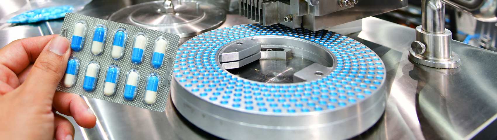 Hand holding blue capsule pack at medicine pill production line, Industrial pharmaceutical concept.banner side